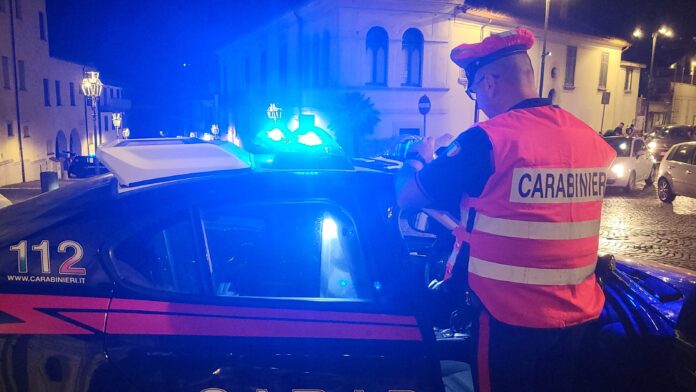 Carabiniere con giubbotto rifrangente in servizio accanto ad auto dei Carabinieri con lampeggianti accesi di notte a Solofra