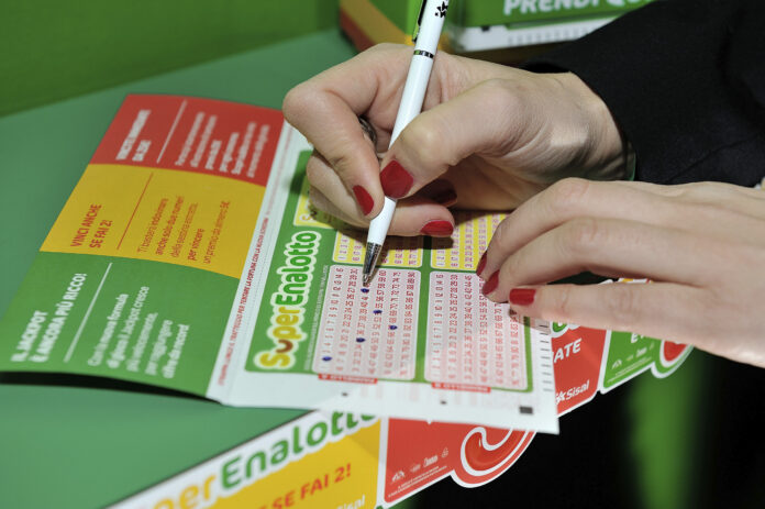 Mano che compila una schedina del SuperEnalotto con una penna su un piano verde.