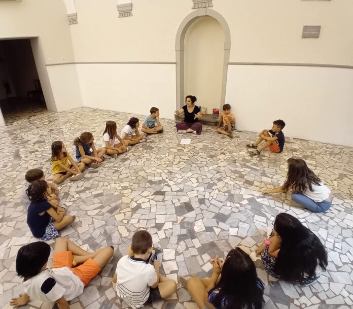 Gruppo di bambini seduti in cerchio durante un laboratorio teatrale.