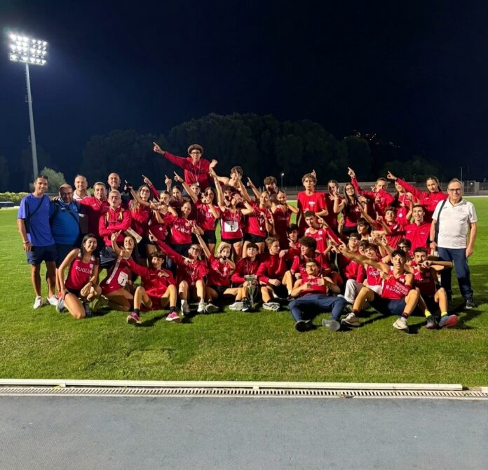 Foto di gruppo della rappresentativa pugliese di atletica Under 16 sul campo da atletica di notte con maglie rosse.