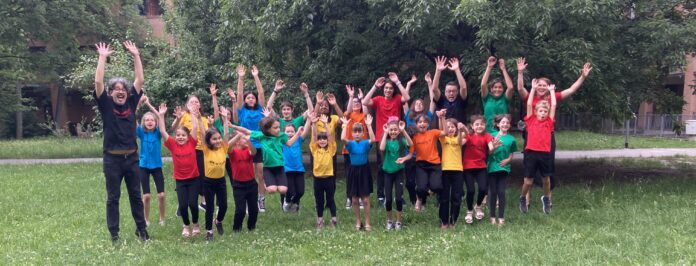 Gruppo di bambini e ragazzi che saltano in un prato verde con gli psicologi, indossando magliette colorate.