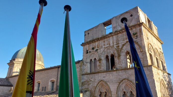 Veduta del centro storico di Gangi con due bandiere davanti a un edificio storico in pietra.