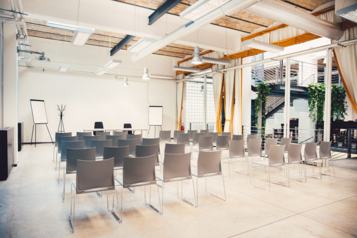 Sala conferenze moderna con sedie disposte in file, luci naturali e arredi contemporanei.