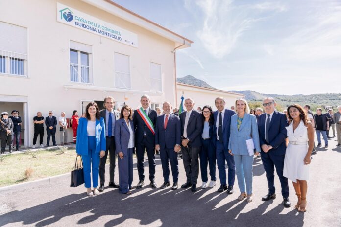Partecipanti alla cerimonia di inaugurazione della Casa e Ospedale di Comunità a Guidonia Montecelio, in piedi davanti all'edificio con insegna.