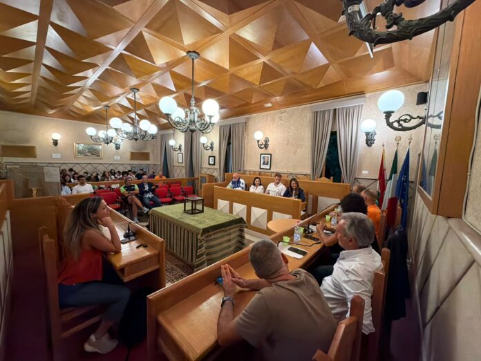 Foto illustrativa della presentazione della stagione sportiva 2026/2027 dell'Asd Dynamica in una sala consiliare affollata, persone sedute e relatori al tavolo.