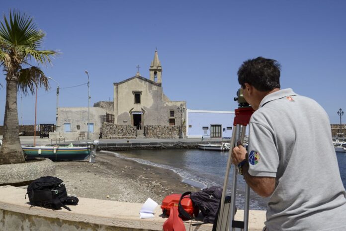 Ricercatore mentre effettua rilievi topografici con strumento ottico in corrispondenza di una chiesetta a Lipari Marina Corta
