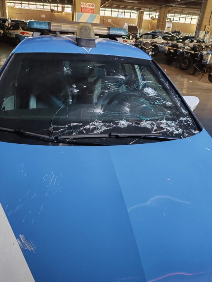 Parabrezza di un'auto della polizia gravemente danneggiato in un parcheggio con altri veicoli di polizia