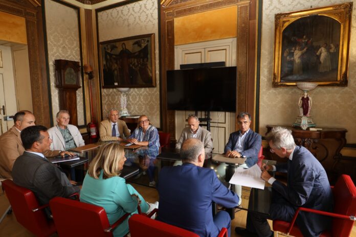 Riunione di lavoro con persone sedute attorno a un tavolo in una stanza elegante con quadri alle pareti, immagini di archivio illustrative della firma del protocollo Osservatorio Salute Bagnoli.