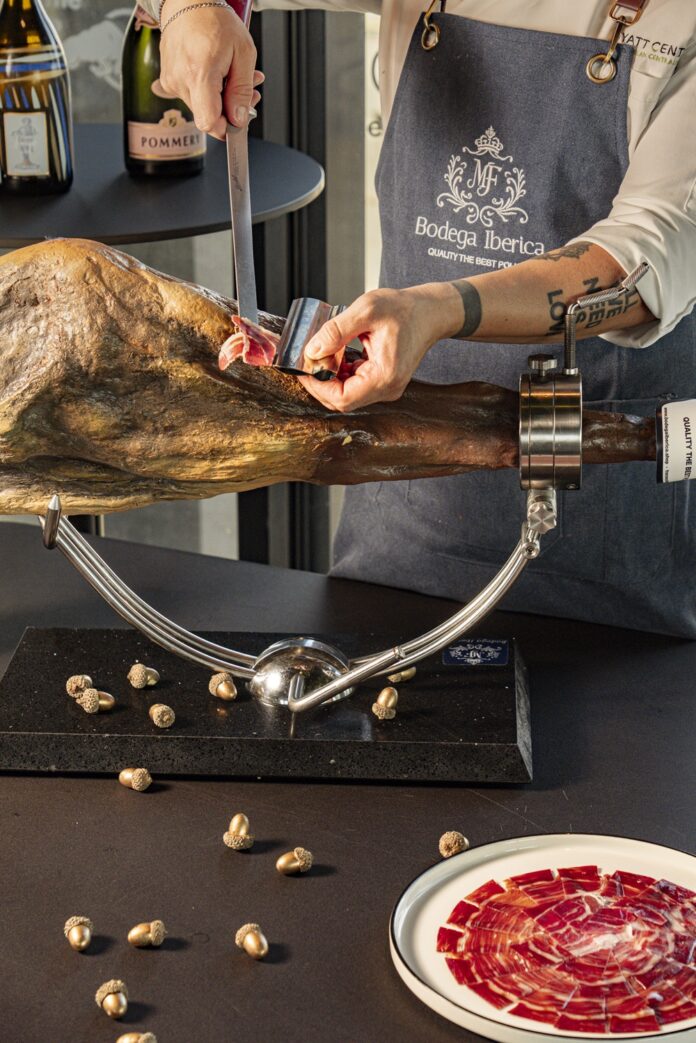 Tavolo con piatto di prosciutto Pata Negra, bicchieri di champagne, bottiglia di champagne e grissini su un piatto, ambiente elegante con luce naturale.