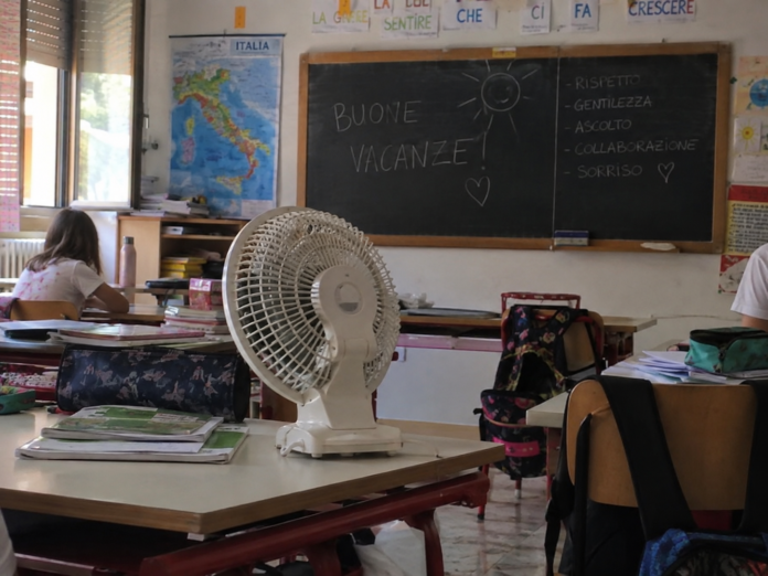 Ventilatore su un banco in una classe scolastica con lavagna e materiale didattico.