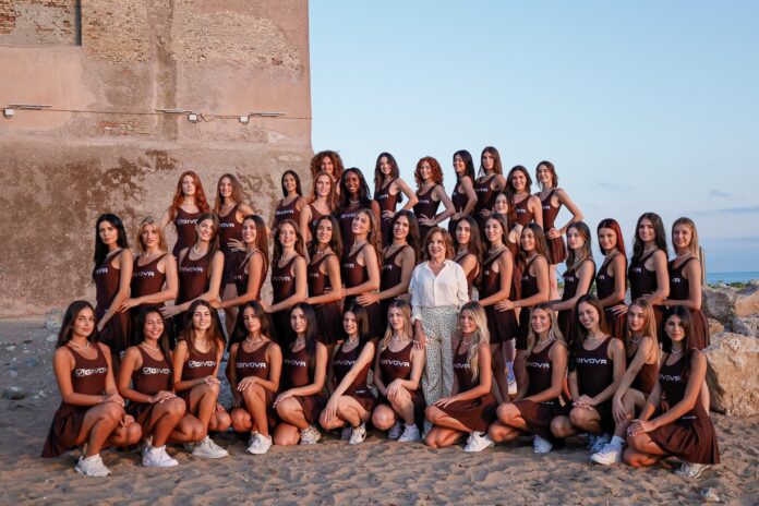 Gruppo di ragazze concorrenti alla docu-serie Miss Italia, la sfida oltre la bellezza, ritratte in posa all'aperto davanti a un muro di pietra con il mare sullo sfondo, indossando abiti coordinati.