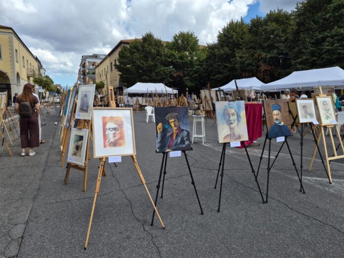 Esposizione all'aperto con quadri su cavalletti durante l'evento artistico Aprilia Arte in Libertà