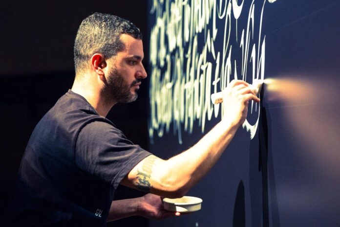 Artista Luca Barcellona durante una performance di calligrafia live su un muro
