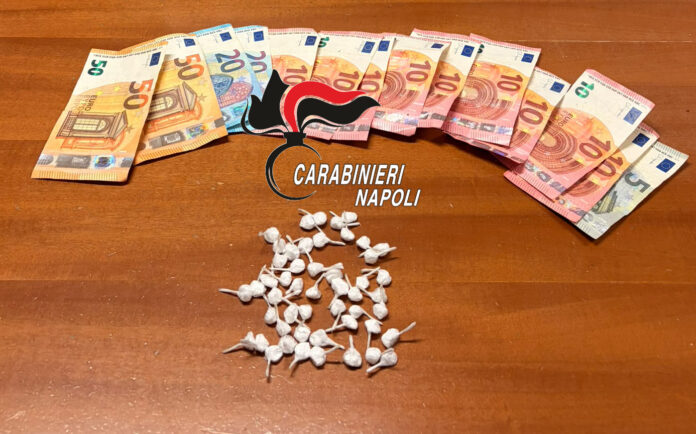 Dosi di cocaina in piccoli involucri e banconote su un tavolo con il logo dei carabinieri di Napoli.