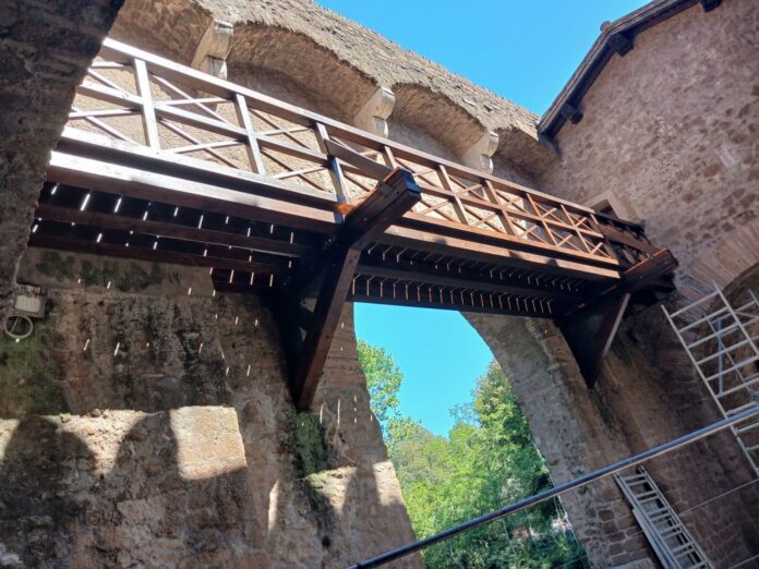 Passerella storica in legno ripristinata tra le due torri di Ponte Nomentano, vista dal basso tra le mura in pietra del ponte.