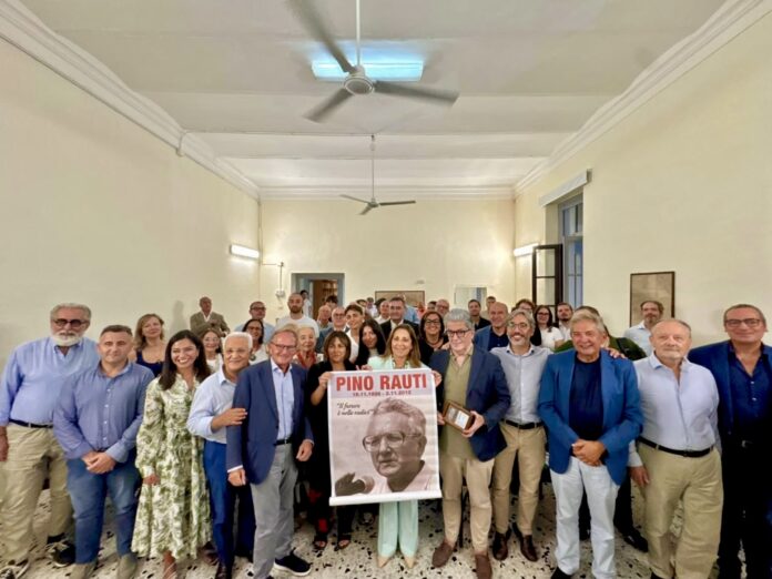 Foto di gruppo in interno durante un convegno con persone che tengono un manifesto commemorativo di Pino Rauti.