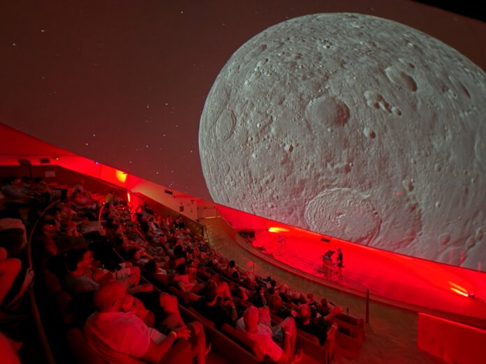 Visita guidata al museo scientifico interattivo con operatore che spiega a un gruppo di adulti e bambini.