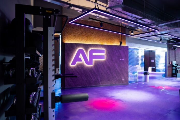 Interno di una palestra con il logo luminoso AF sul muro, attrezzature da palestra e illuminazione moderna.