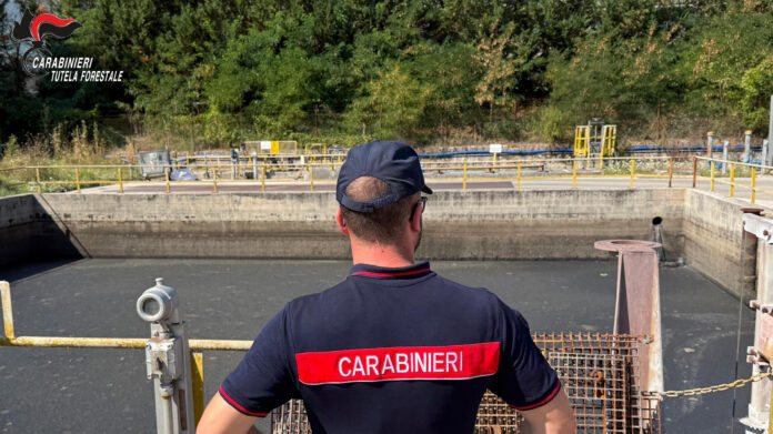 Impianto di depurazione con vasca di trattamento vista dall'alto, con una persona in divisa dei Carabinieri in primo piano di spalle.
