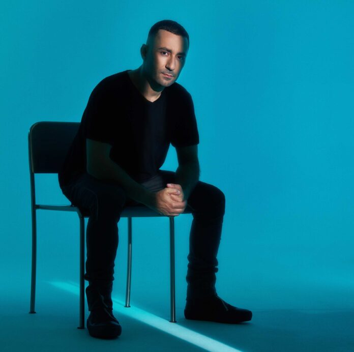 Ritratto promozionale di Joseph Capriati seduto su una sedia in uno sfondo blu.