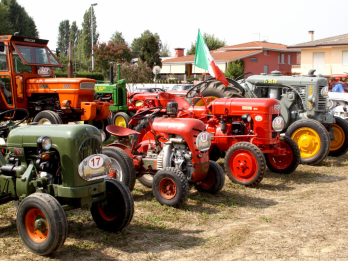 Trattori d'epoca di diversi colori in esposizione all'aperto.