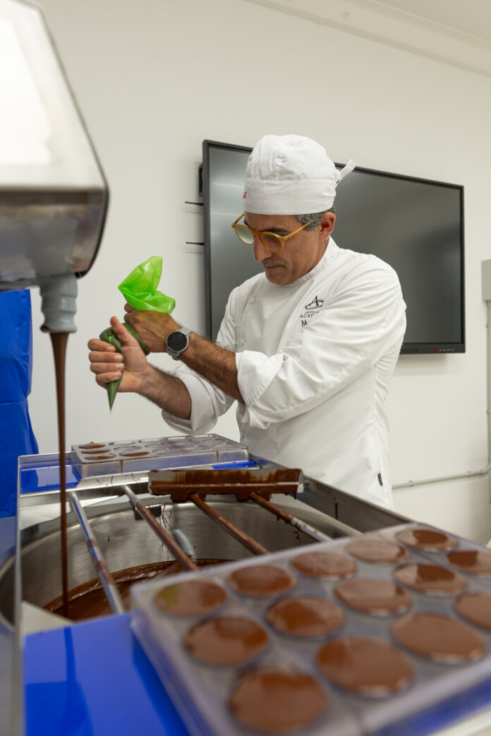Persona vestita in camice bianco e cuffia protettiva mentre lavora con cioccolatini in una macchina automatica in un laboratorio agroalimentare moderno.