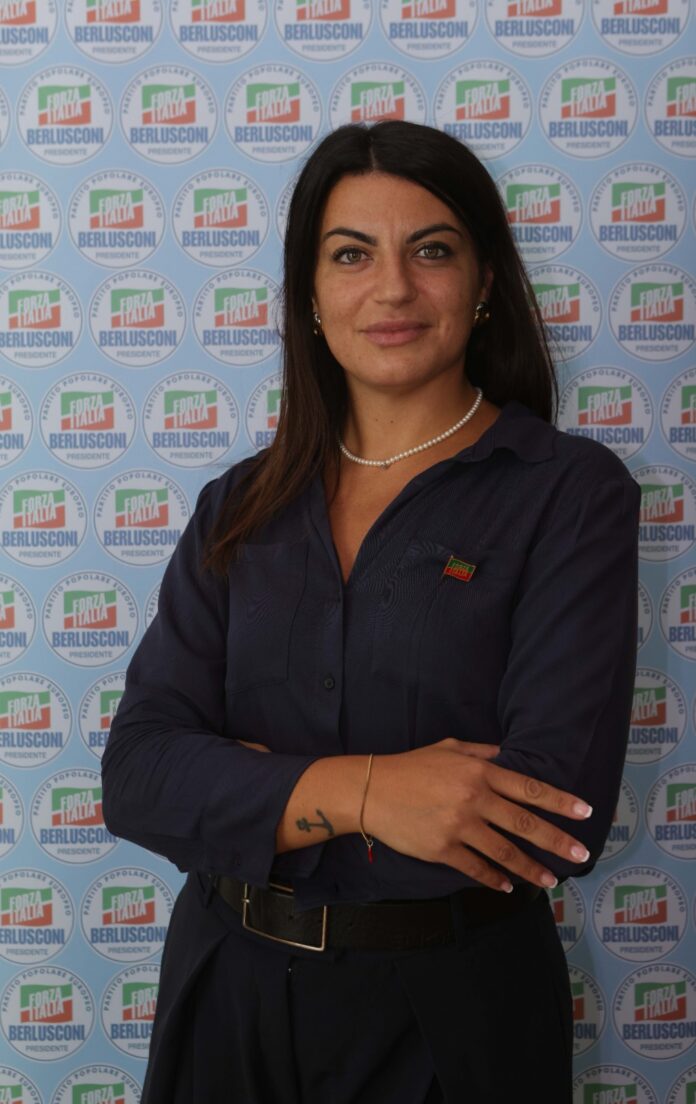 Donna in abbigliamento formale davanti a una parete con loghi di Forza Italia.