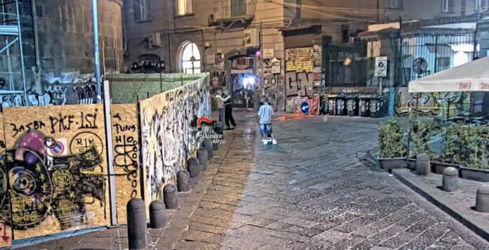 Piazza del Gesù a Napoli di sera con personaggi in lontananza e muri con graffiti.