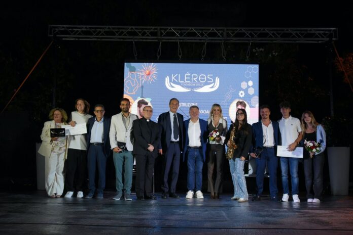 Gruppo di persone sul palco durante una serata di premiazione sotto un grande schermo con il logo della Fondazione Klêros