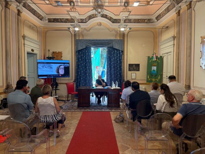 Sala con persone sedute di fronte a un tavolo dove si tiene una riunione con presentazione su schermo.