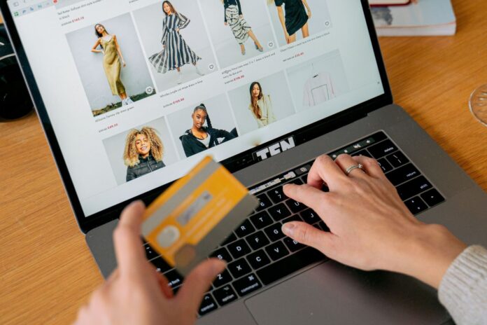 Persona che acquista vestiti online su un laptop tenendo una carta di credito in mano.