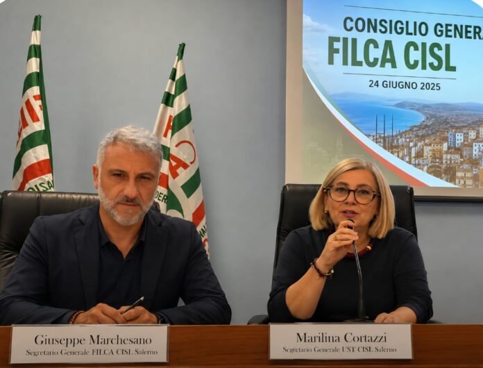 Marilina Cortazzi e Giuseppe Marchesano seduti a un tavolo durante un incontro sindacale con bandiere CISL sullo sfondo.