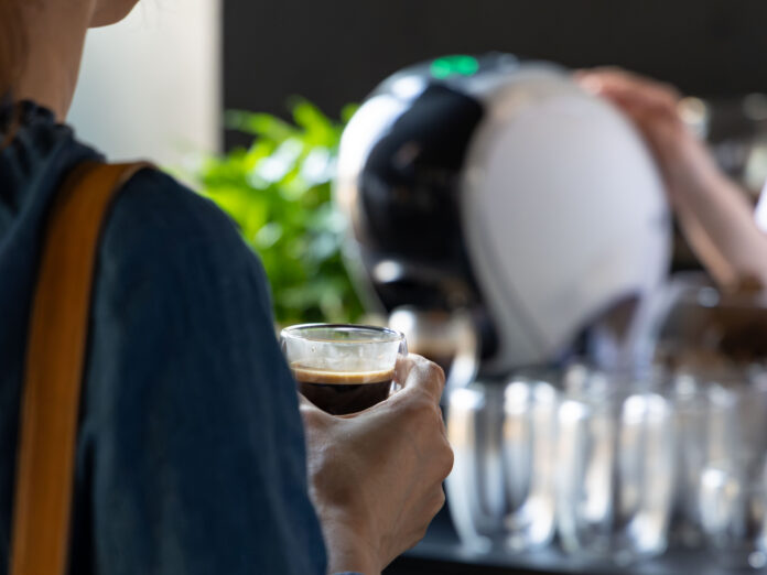 Persona che prepara un caffè con una macchina a capsule domestica, tenendo una tazzina in mano