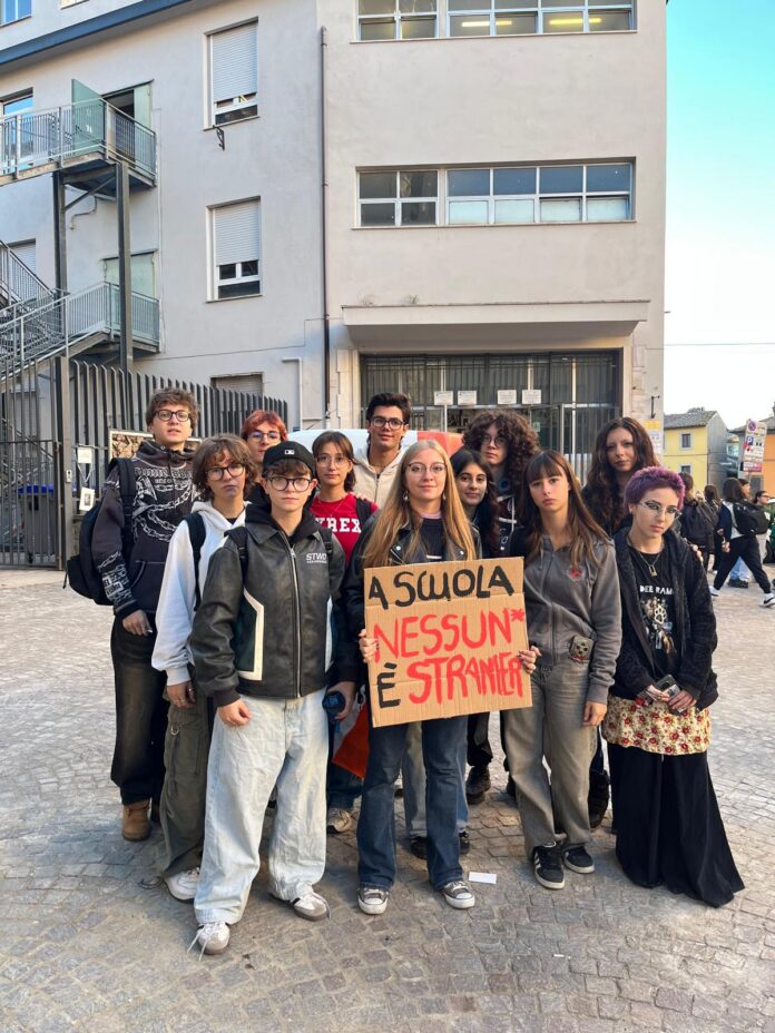 Studenti su una scalinata di una scuola con uno striscione contro discriminazioni nella scuola pubblica