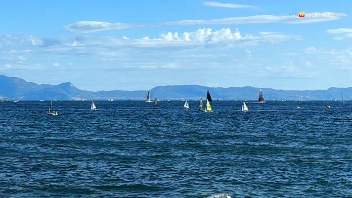 Barche a vela sul mare di Napoli con lo sfondo del lungomare e montagne.