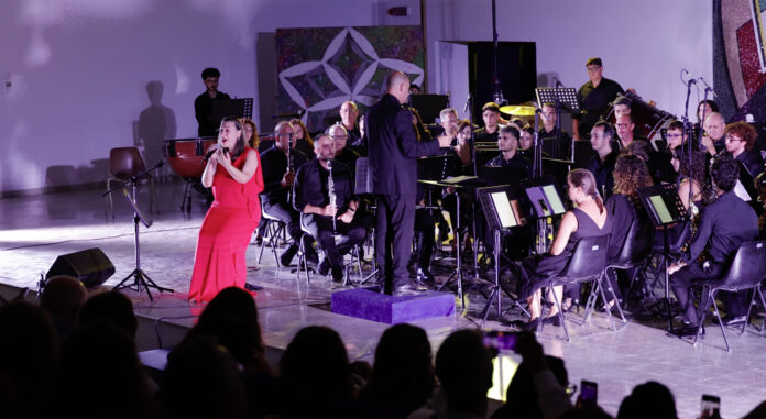 Concerto con Daria Biancardi in abito rosso e banda musicale durante esibizione a Gibellina