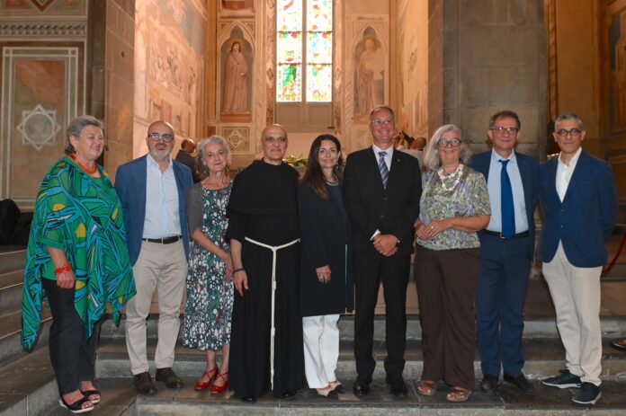 Un gruppo di nove persone in piedi all'interno della Basilica di Santa Croce, con pareti affrescate e una finestra colorata sullo sfondo.