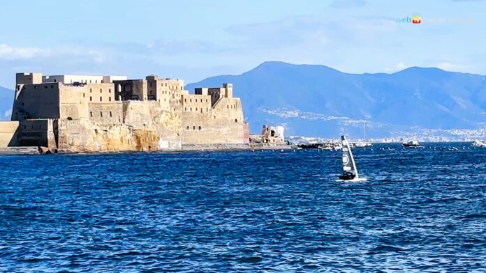 Barca a vela in acqua con il Castel dell'Ovo sullo sfondo e montagne in lontananza, Napoli.