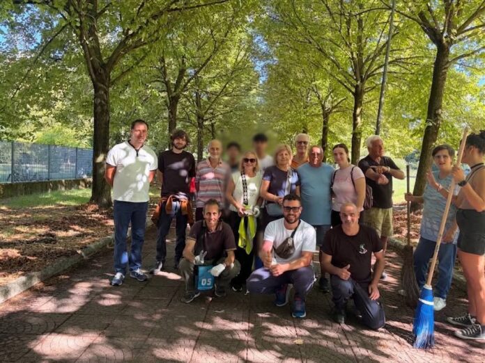Volontari riuniti in un parco alberato a San Basilio, Roma, durante un'attività di pulizia del verde pubblico.