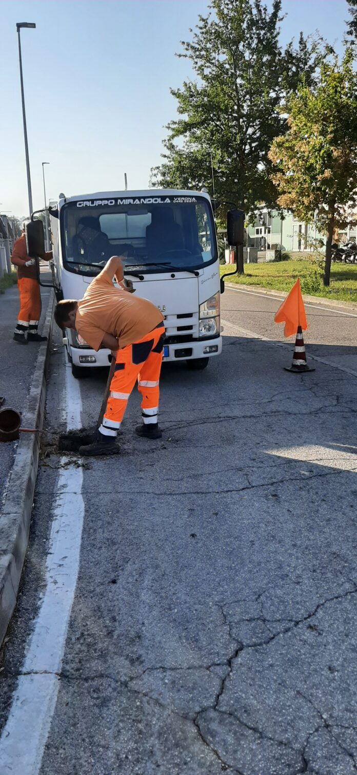 Operatori al lavoro per la pulizia delle caditoie lungo una strada urbana con un camion di servizio.