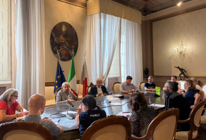 Sala riunioni con persone sedute attorno a un tavolo durante un incontro istituzionale a Forlì