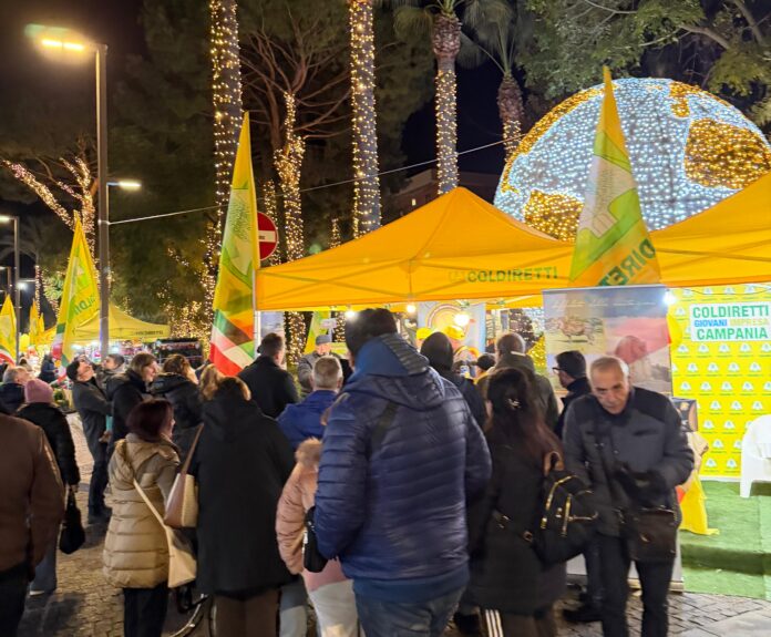 Persone a un mercato contadino serale con gazebo gialli e luci sugli alberi, evento Notti Gialle Coldiretti a Sorrento