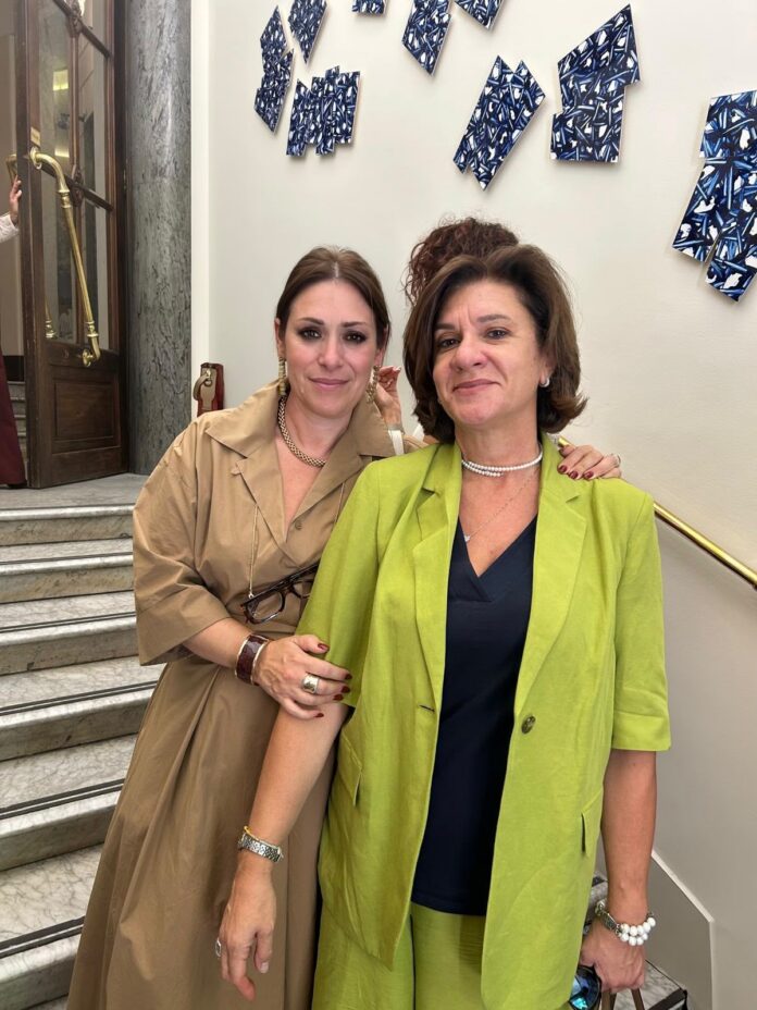 Due donne in un interno con una scalinata e decorazioni murali, immagine allegata al comunicato stampa di Confcommercio.