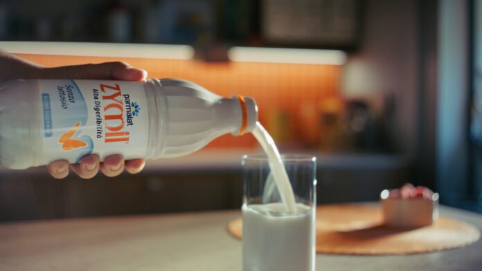 Bottiglia di latte senza lattosio Parmalat Zymil accanto a un bicchiere di latte e una ciotola di cereali in una cucina luminosa, con scritta 'Buongiorno Benessere'.