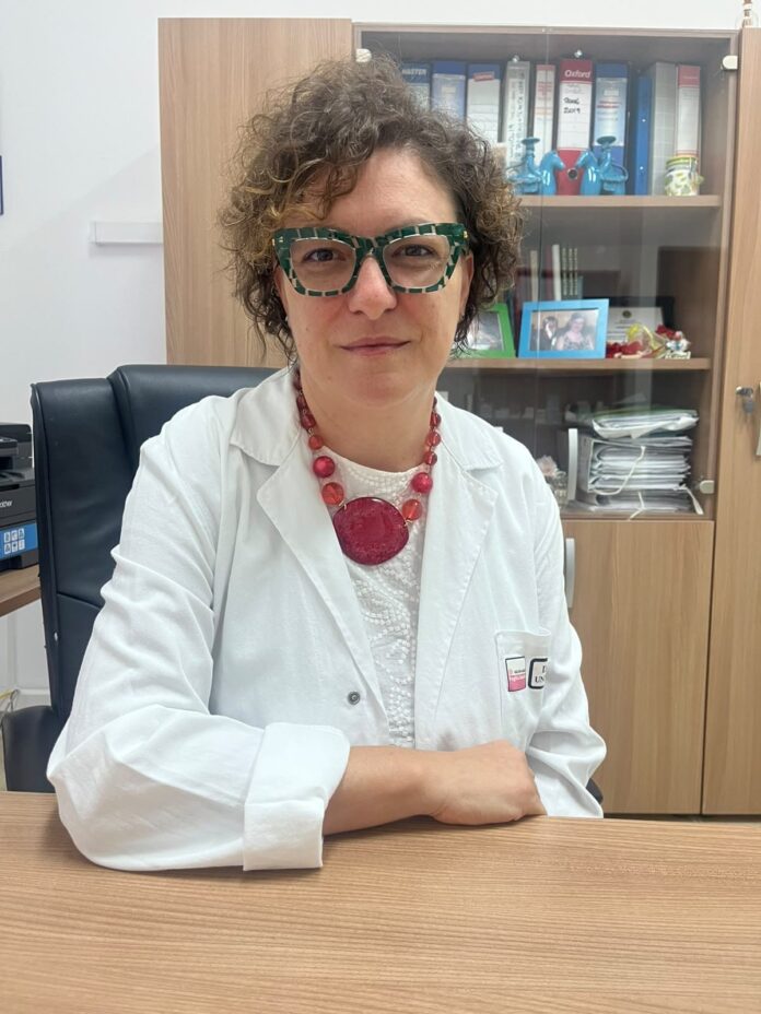 Dottoressa Emanuela Ciracì in camice bianco seduta a una scrivania, immagine illustrativa del congresso sulla malattia epatica steatosica a Ceglie Messapica.