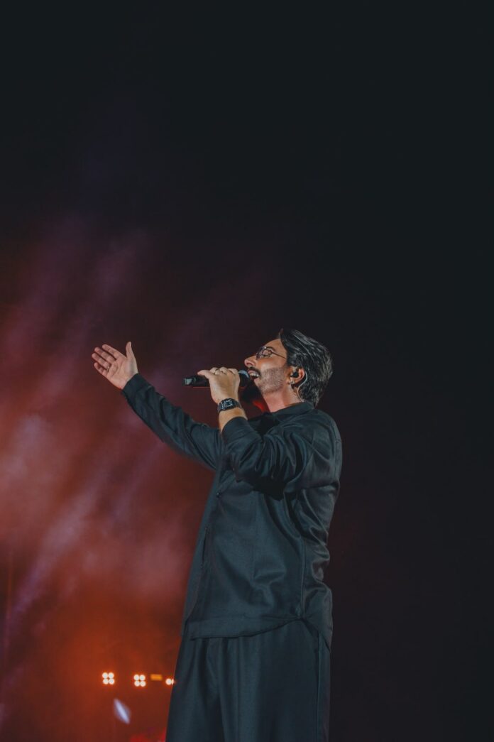 Tony Colombo sul palco durante un concerto con microfono in mano e luci di palcoscenico.