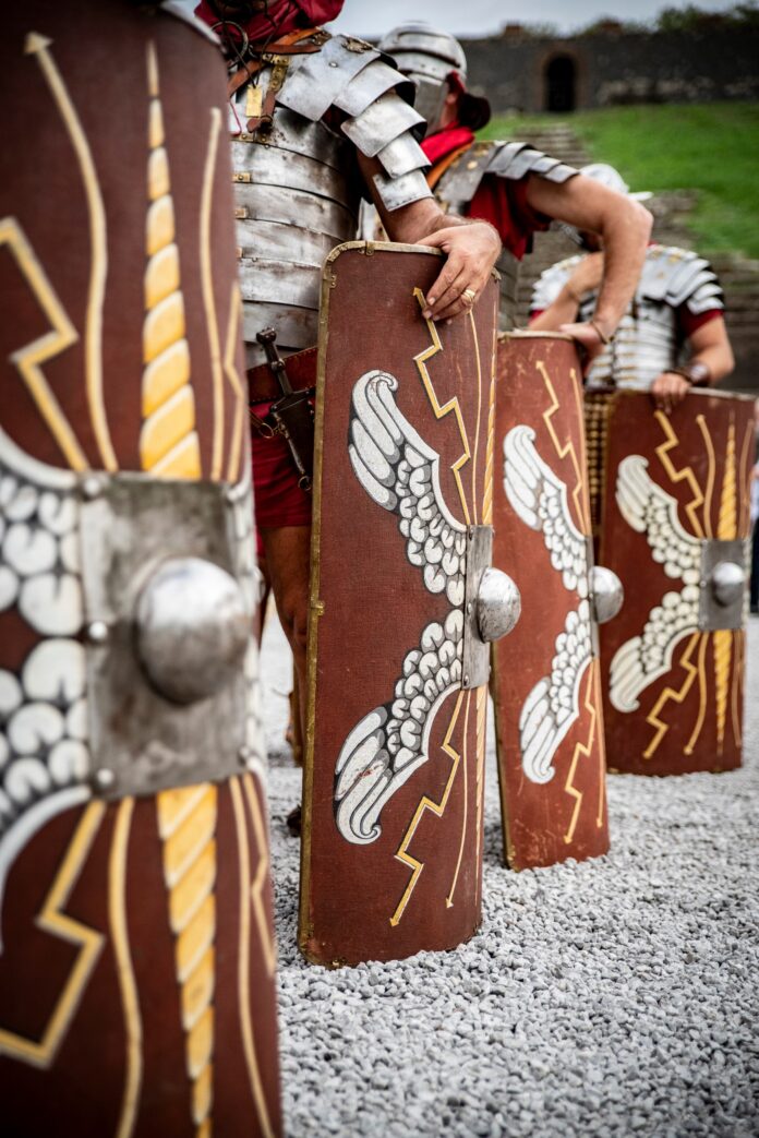 Attori in costumi di gladiatori romani con armature e scudi nel Parco Archeologico di Pompei durante una rievocazione storica.
