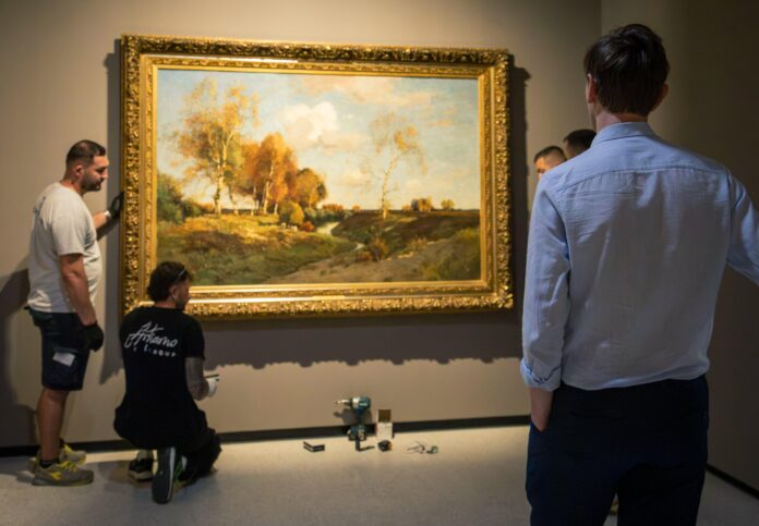 Addetti allestimento che posizionano un quadro in una sala di Palazzo dei Diamanti.