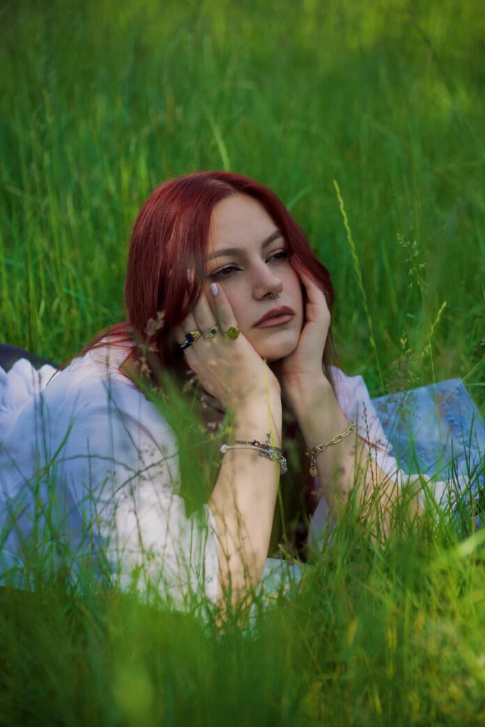 Giovane donna con capelli rossi distesa su un prato verde, immagine illustrativa.