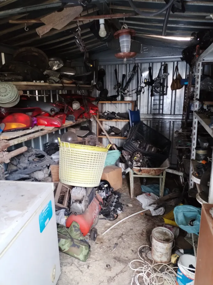 Interno di un locale ingombro di ricambi e parti di veicoli, disposti su scaffali e a terra.